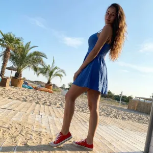 From Behind: Person in a Blue Short Dress and Red Sneakers, Low-Angle Shot with Soft Sunlight Under a Blue Sky