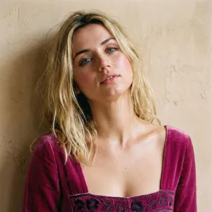 A photo of Ana de Armas with a tousled blonde bob, dewy skin, and magenta velvet top against a warm beige wall